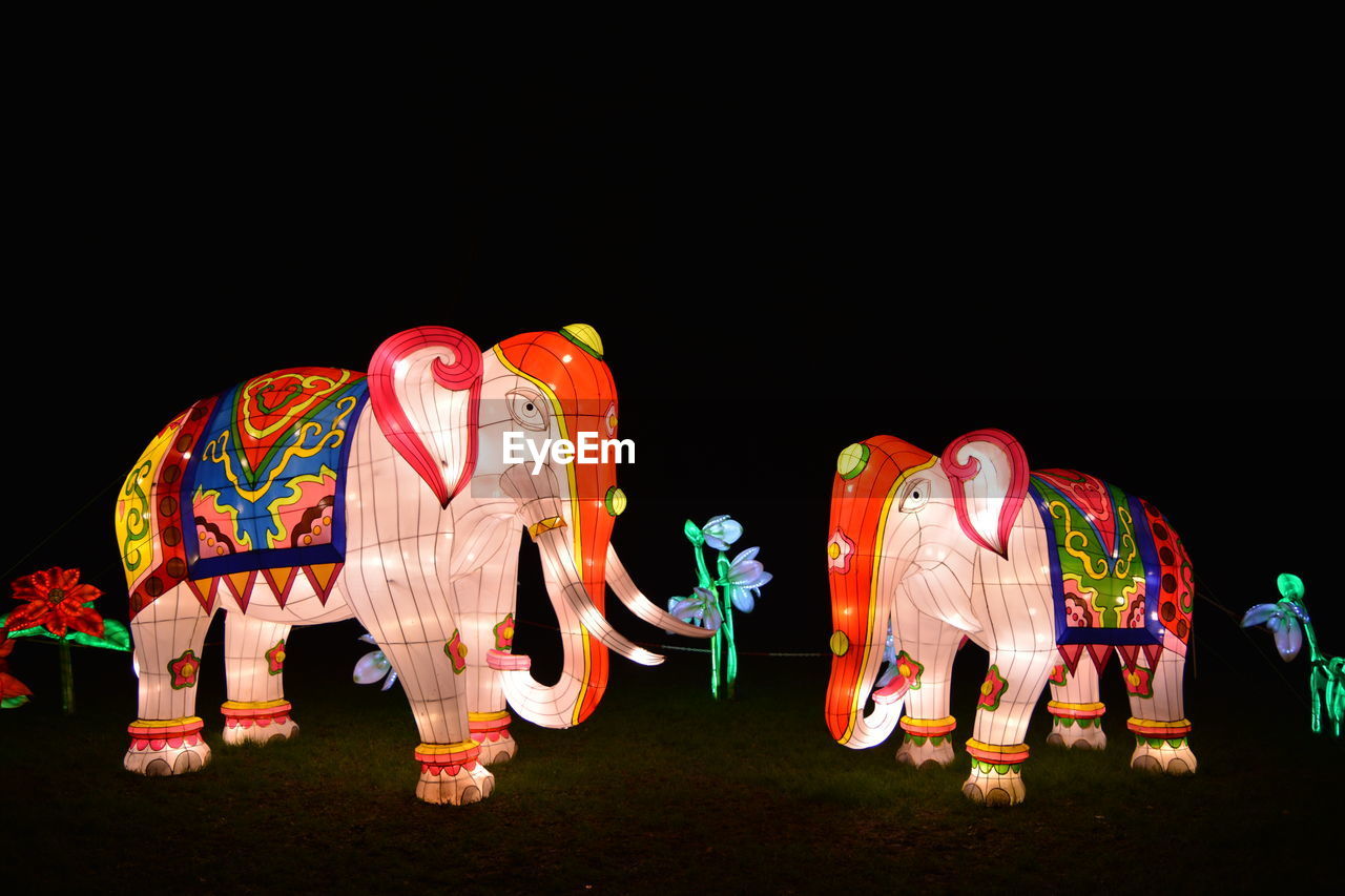 Illuminated elephant figurines on field at night