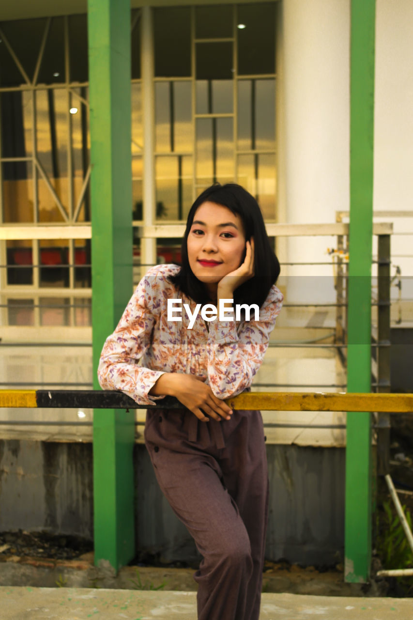 Portrait of smiling young woman standing against built structure