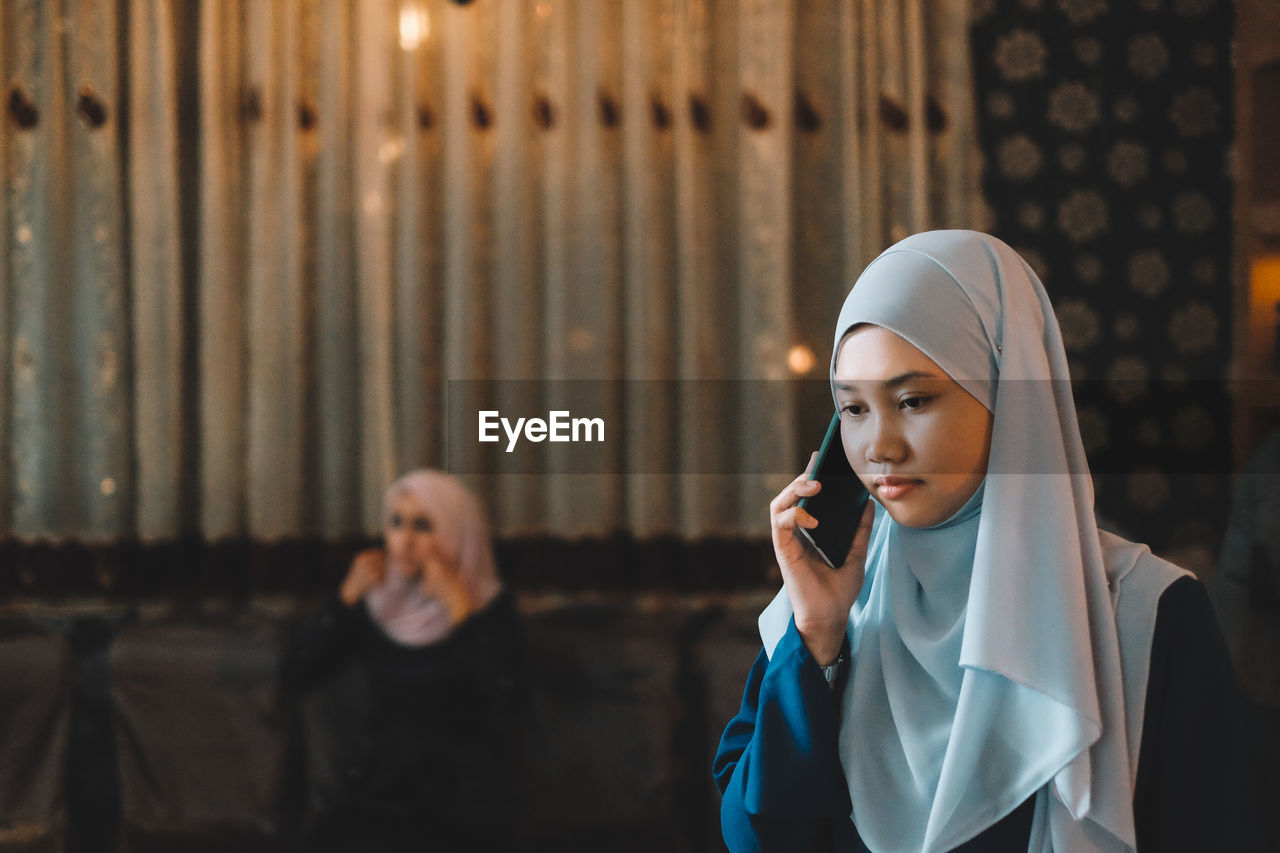 Young woman wearing hijab while answering mobile phone in city