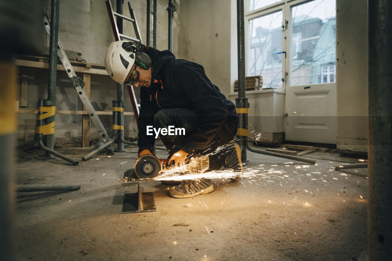 Full length of male construction worker using electric saw while cutting metal at site