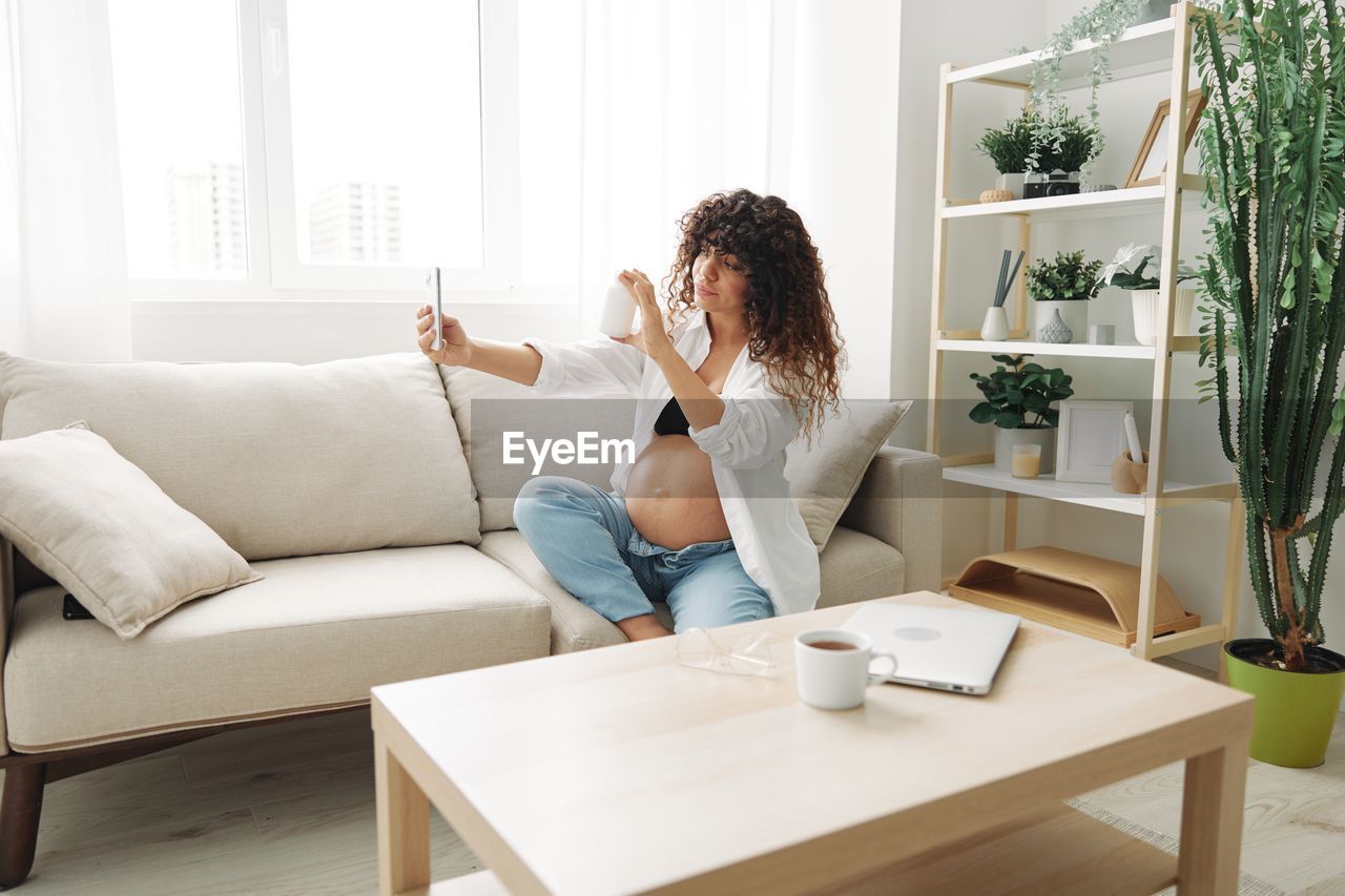 side view of young woman using mobile phone while sitting on sofa at home