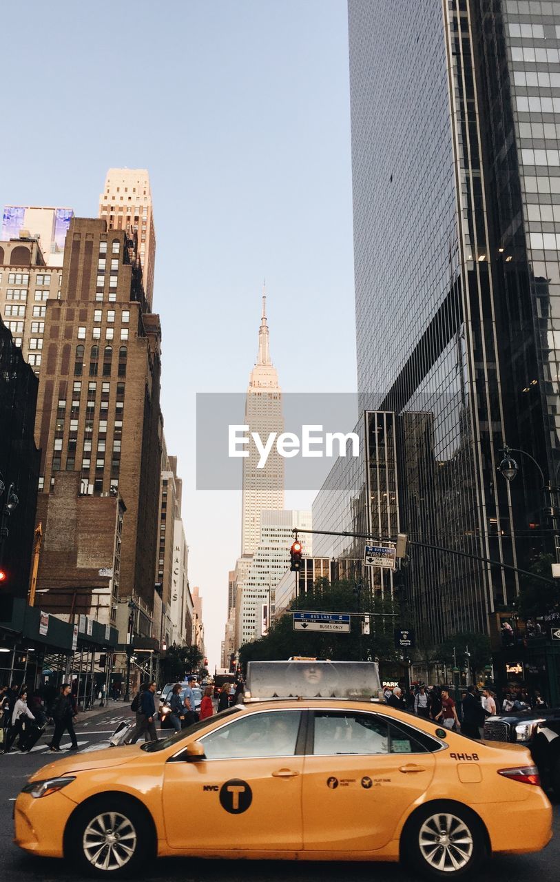 Yellow taxi against empire state building on road in city