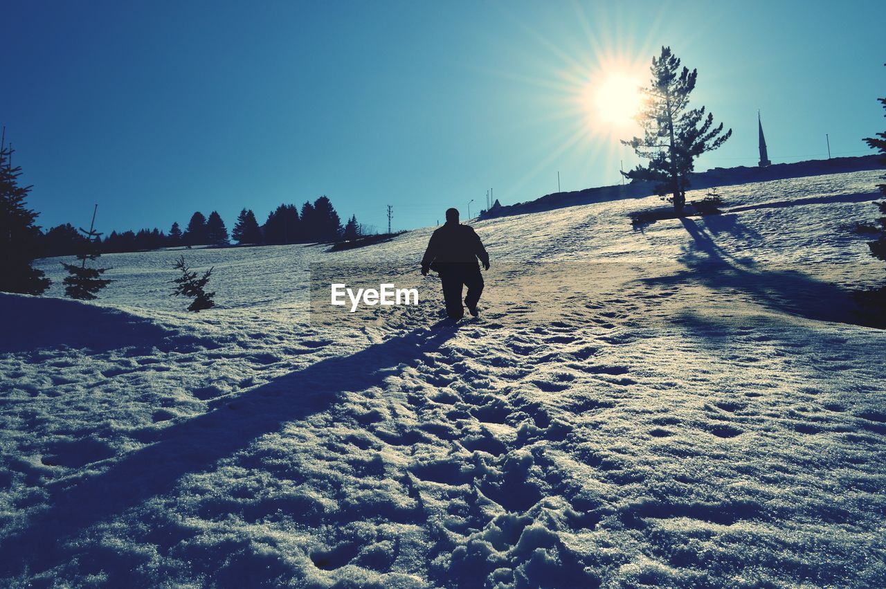 Rear view of silhouette man walking on snow covered landscape