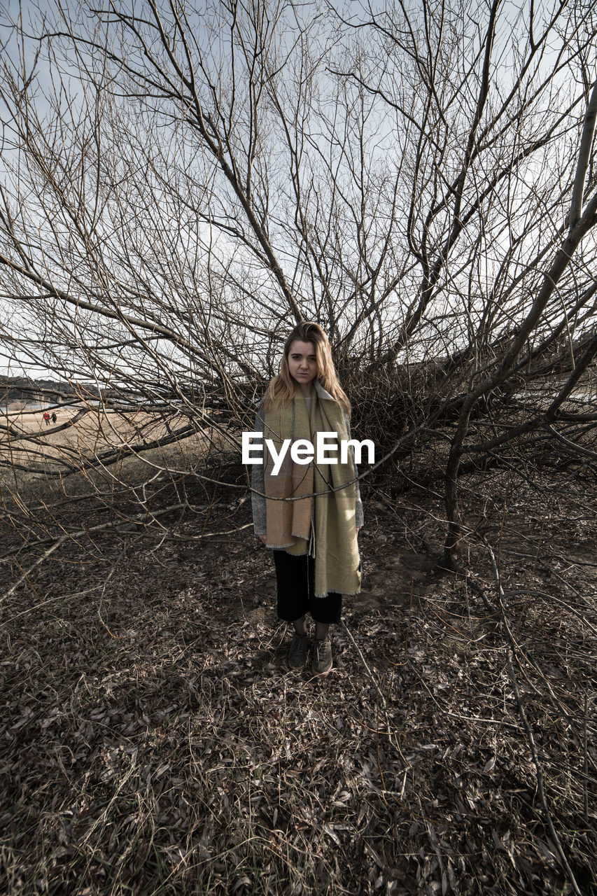 PORTRAIT OF WOMAN STANDING BY BARE TREE