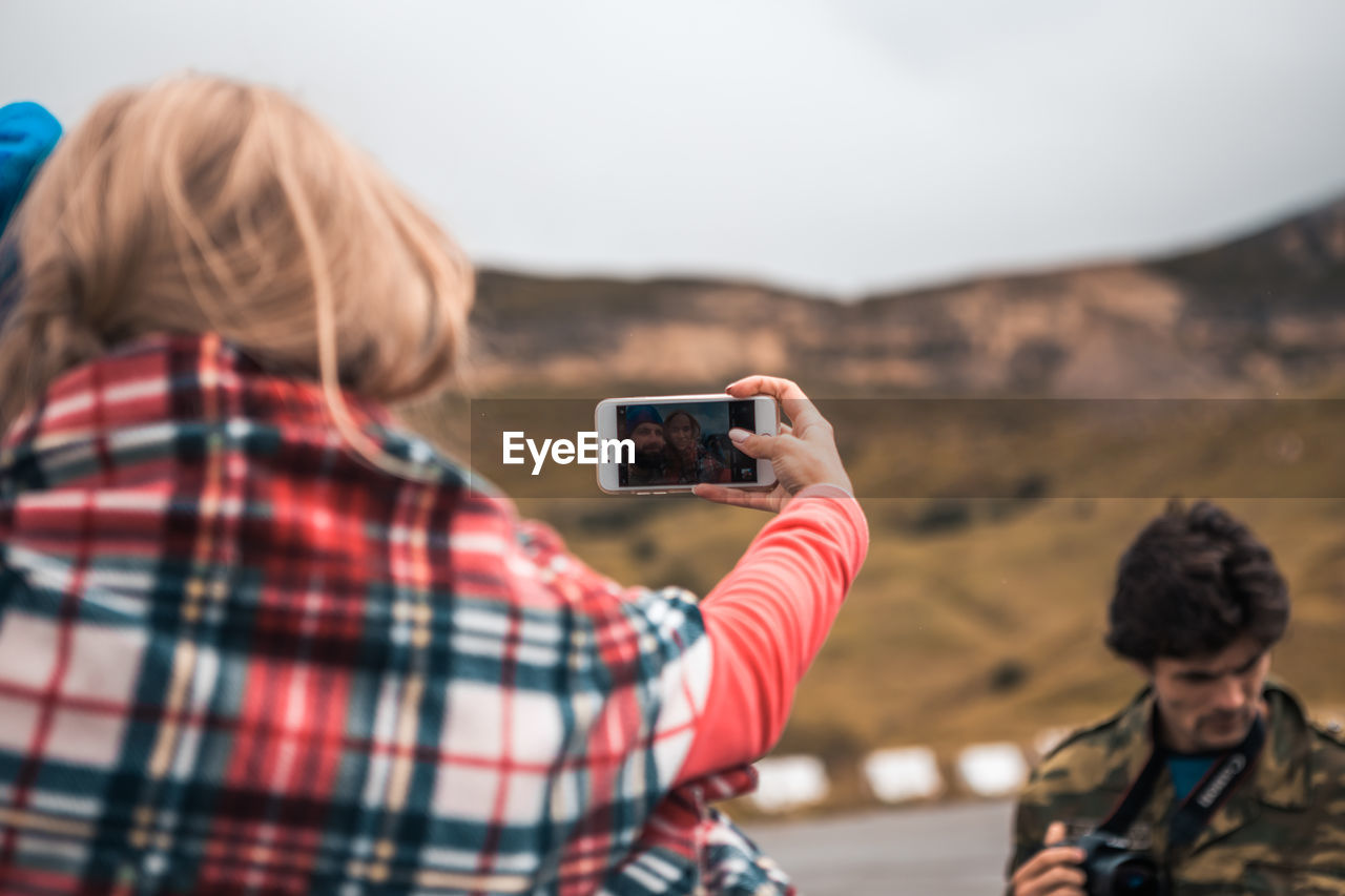 Woman photographing with man on mobile phone while photographer holding camera