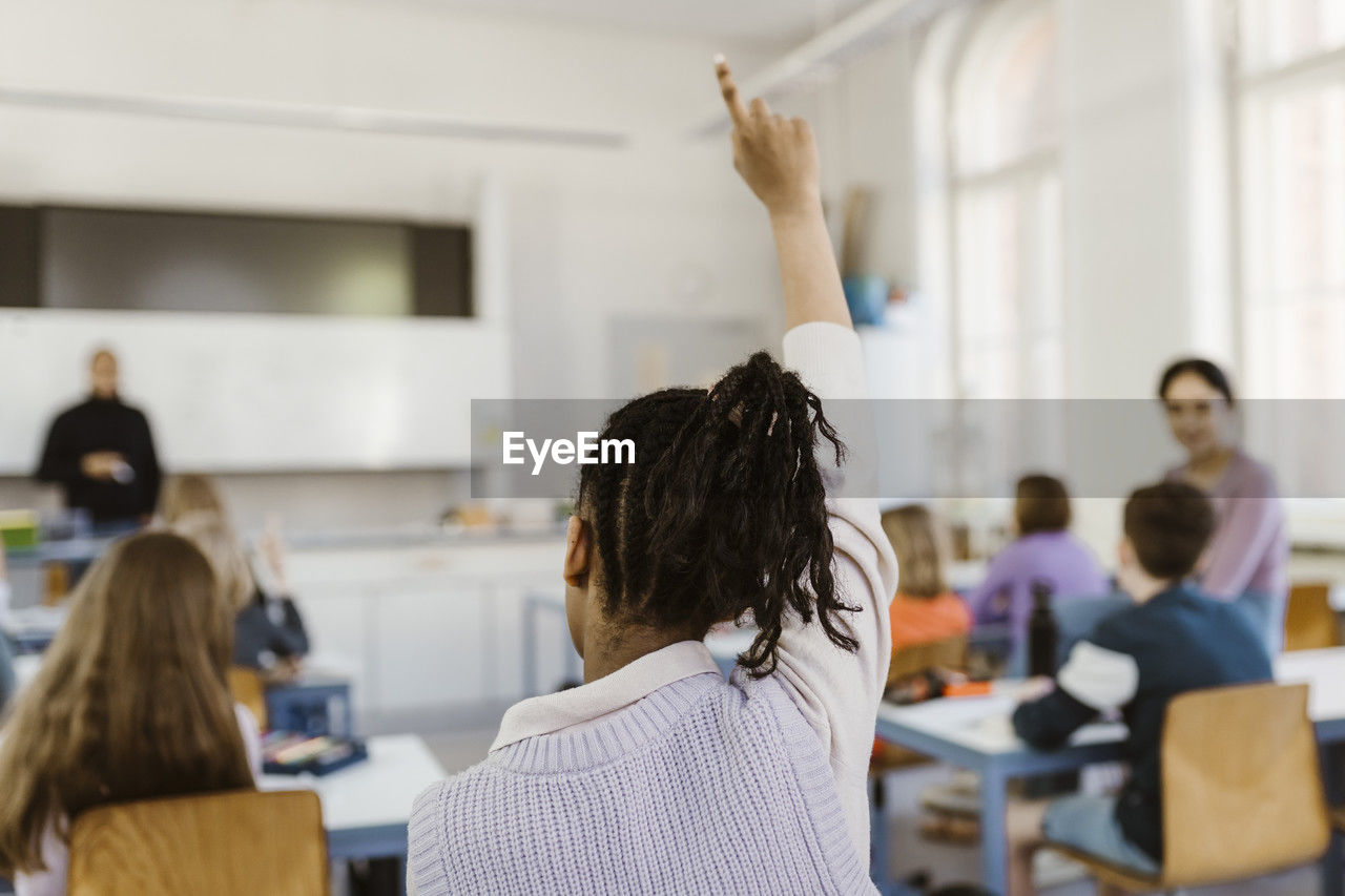 Rear view of female student raising hand during lecture in classroom