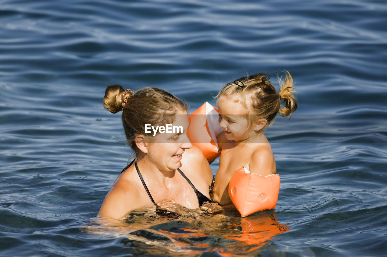 REAR VIEW OF MOTHER AND DAUGHTER IN WATER AT SHORE