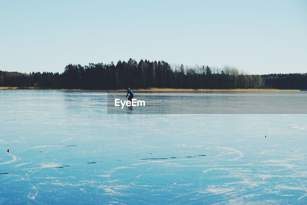 Person ice-skating on frozen lake against clear sky