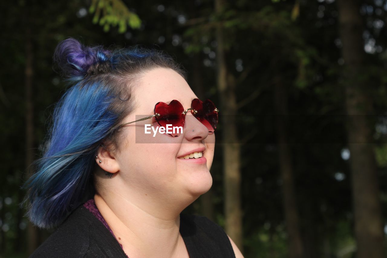 Smiling young woman with blue hair wearing sunglasses in park