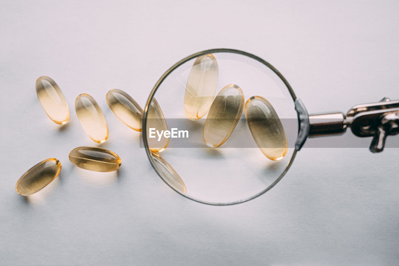 Yellow transparent omega 3 capsules under a magnifying glass. food additive development concept