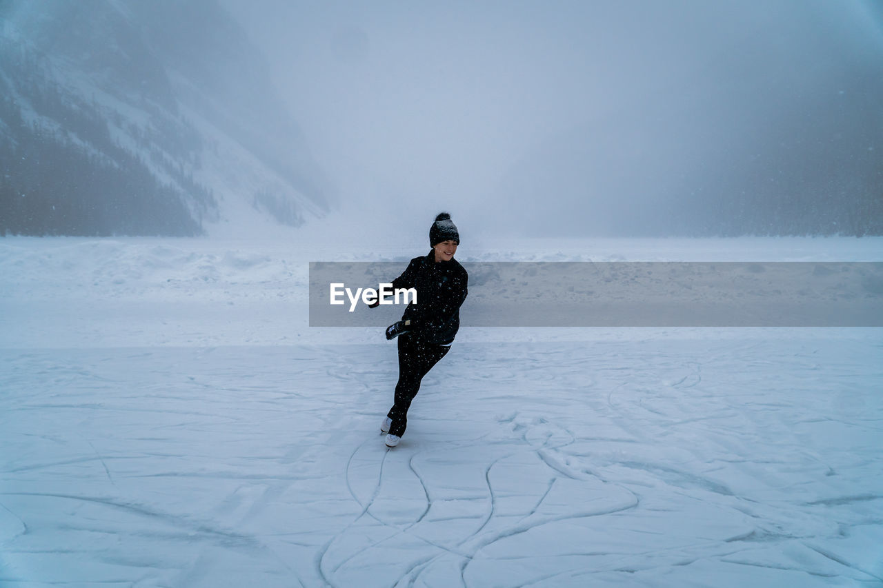 Female ice skater skating on frozen lake outside in snowstorm near forest in canada.