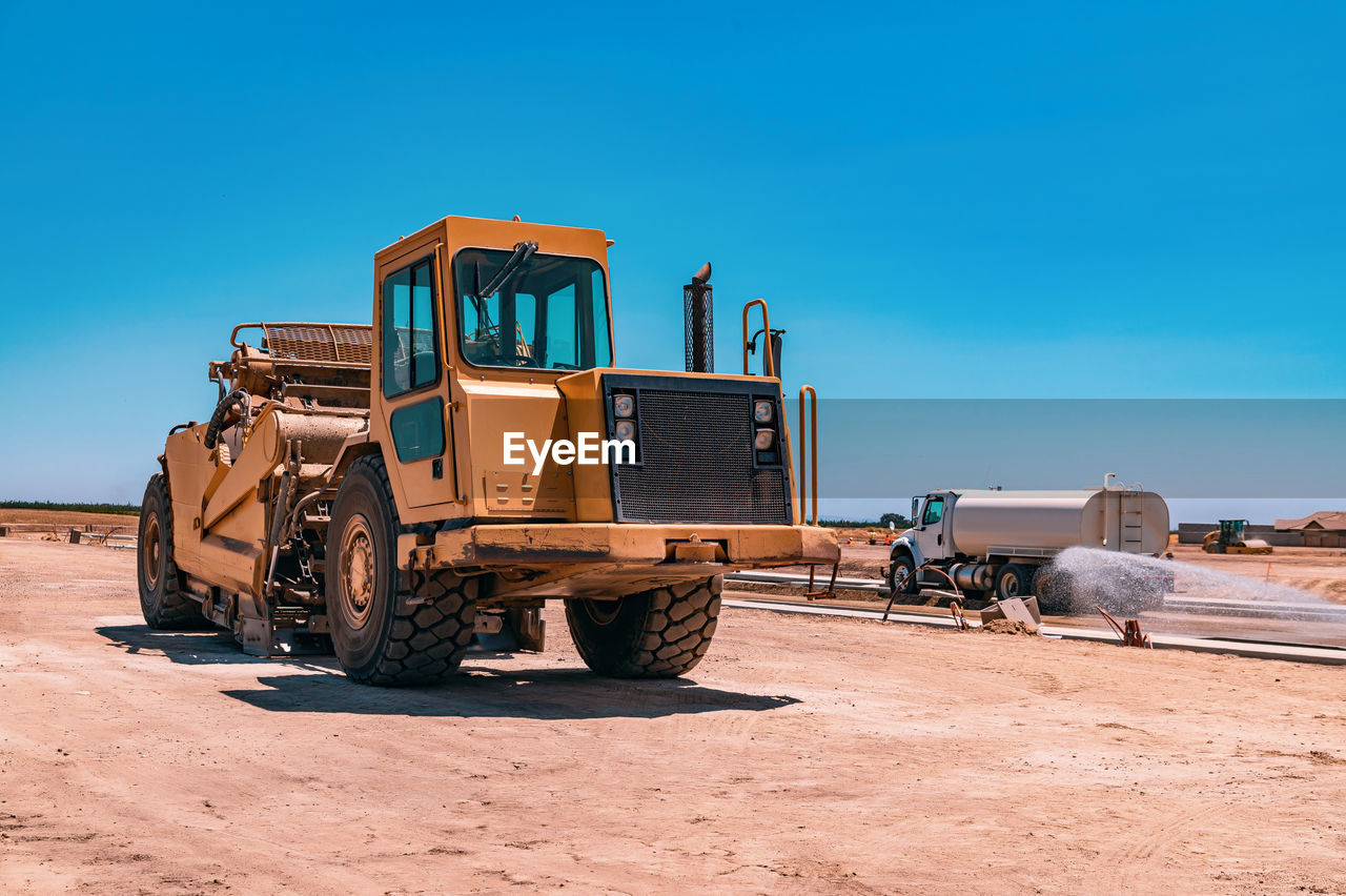 Side view of a large yellow tractor. the watering machine waters the road. 