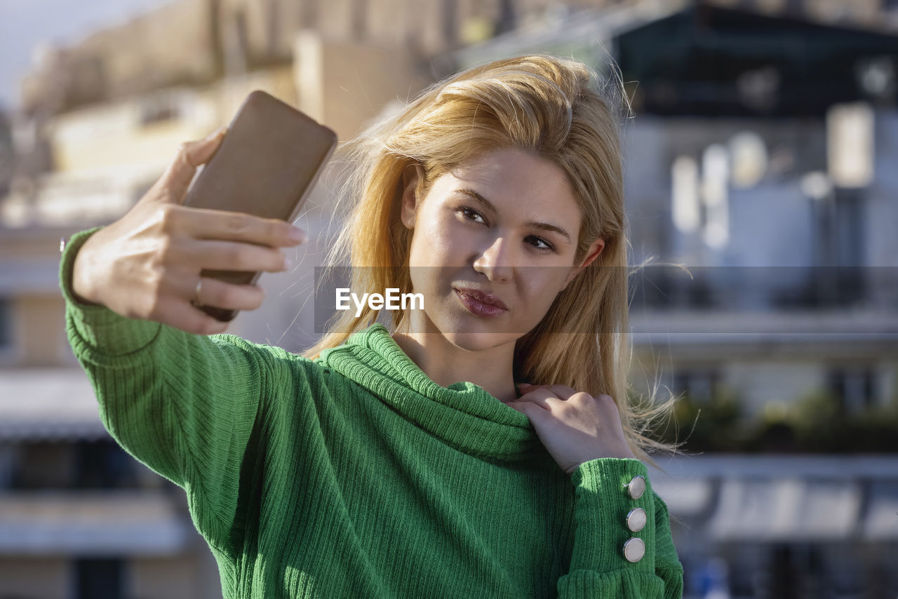 PORTRAIT OF YOUNG WOMAN PHOTOGRAPHING WITH MOBILE PHONE