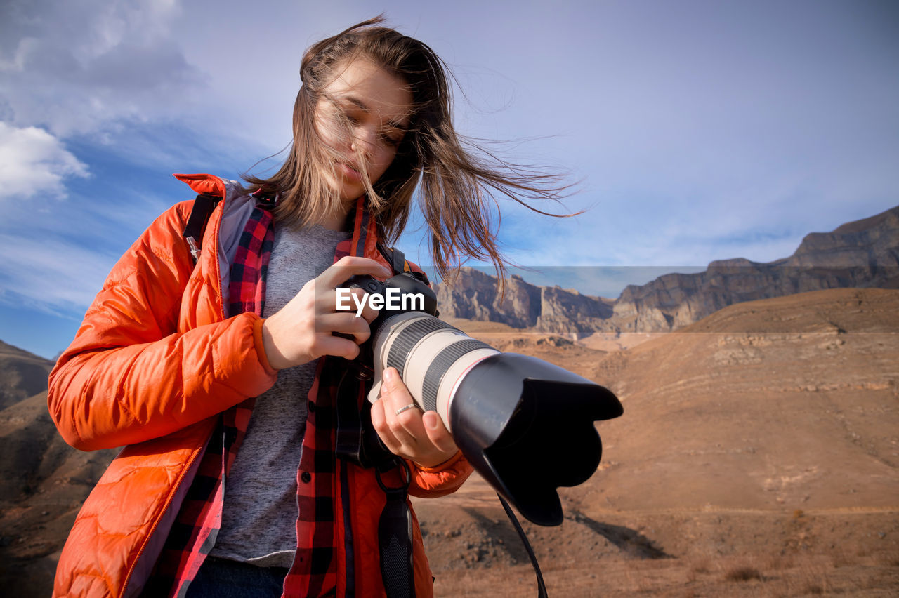 Young hipster woman with a camera in her hands in the mountains in backlight. hair fluttering 