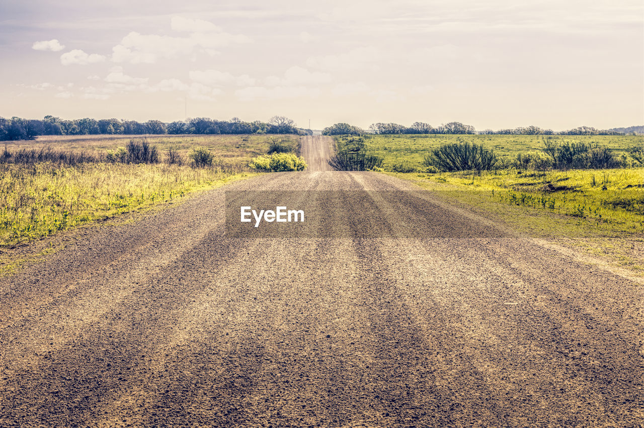 Dirt road amidst field against sky