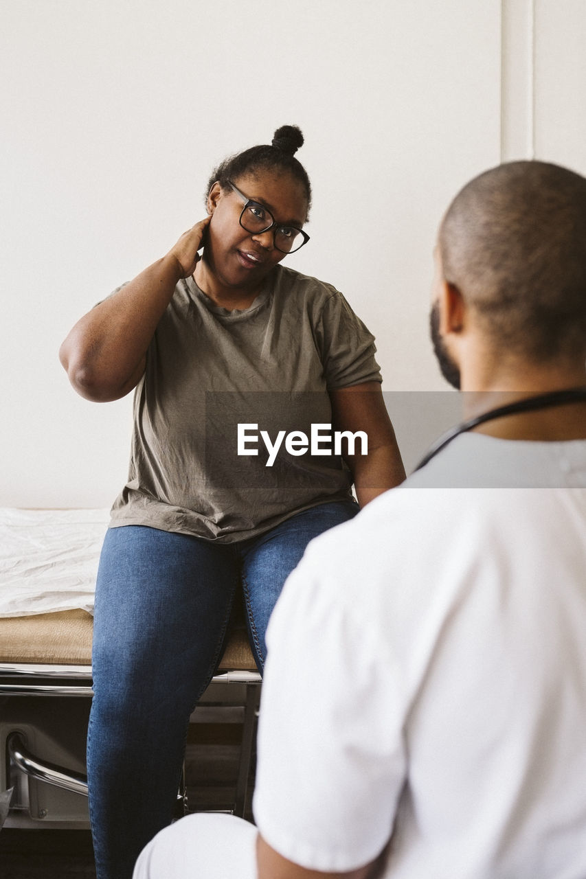 Mid adult woman consulting with male doctor about neck pain at medical clinic