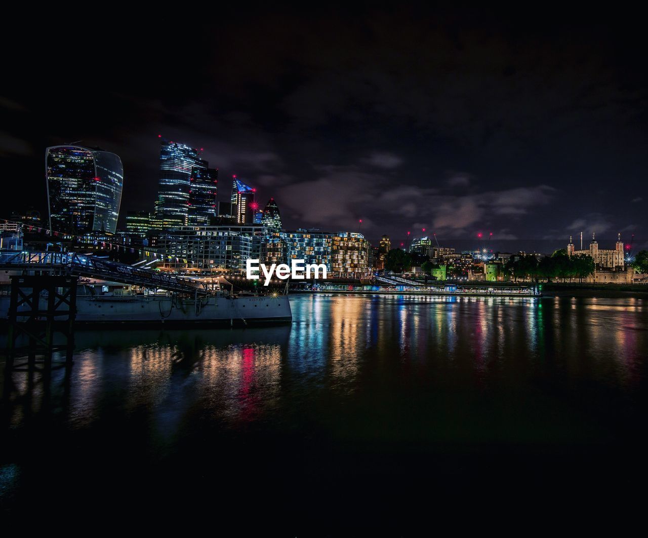 Illuminated buildings by river against sky at night