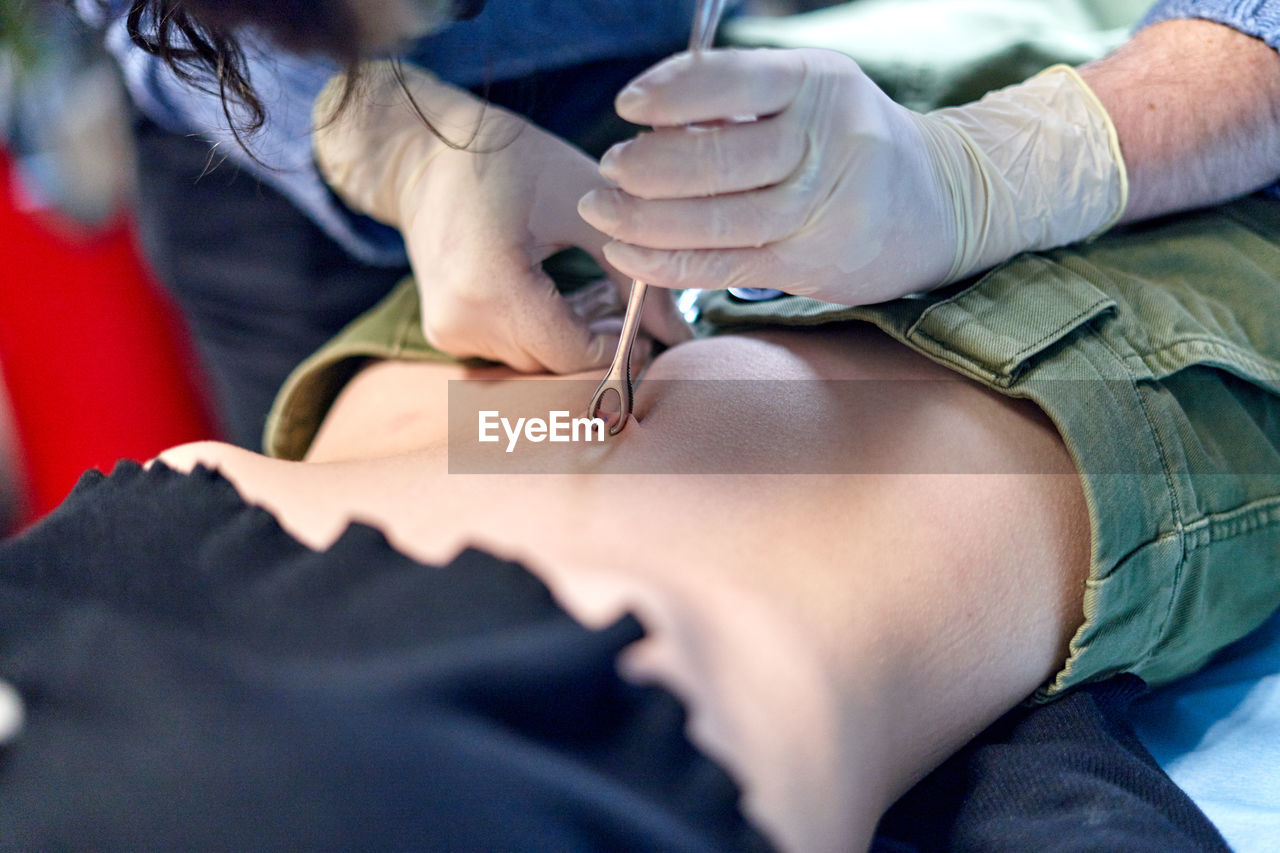 Anonymous body modification artist in glass pinching belly button of female client during piercing procedure in salon