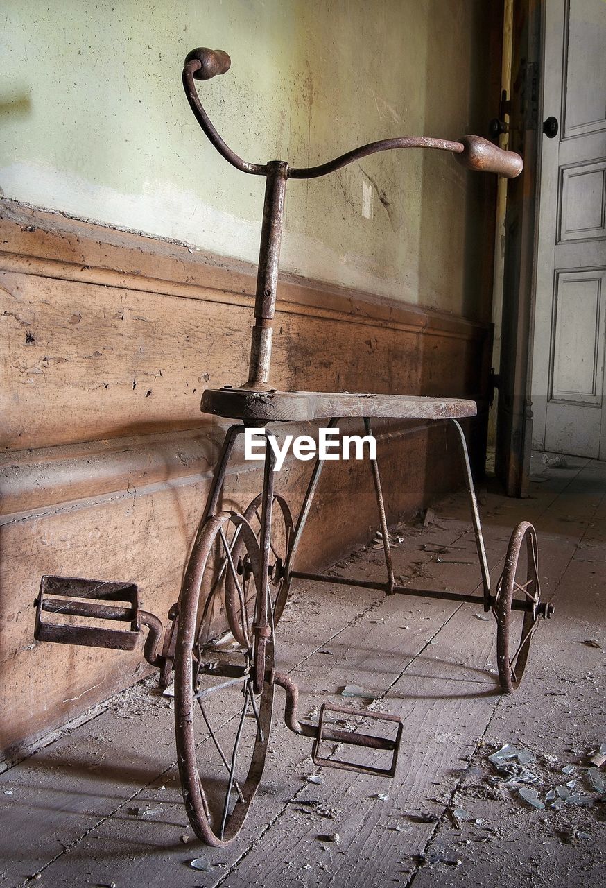 Metallic tricycle on hardwood floor by wall in abandoned home