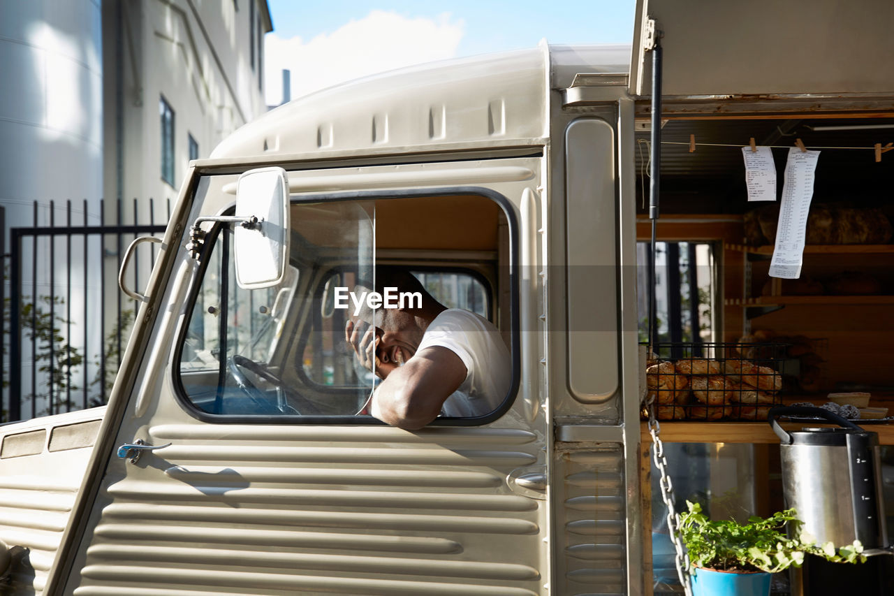 Smiling male owner covering face while sitting in food truck