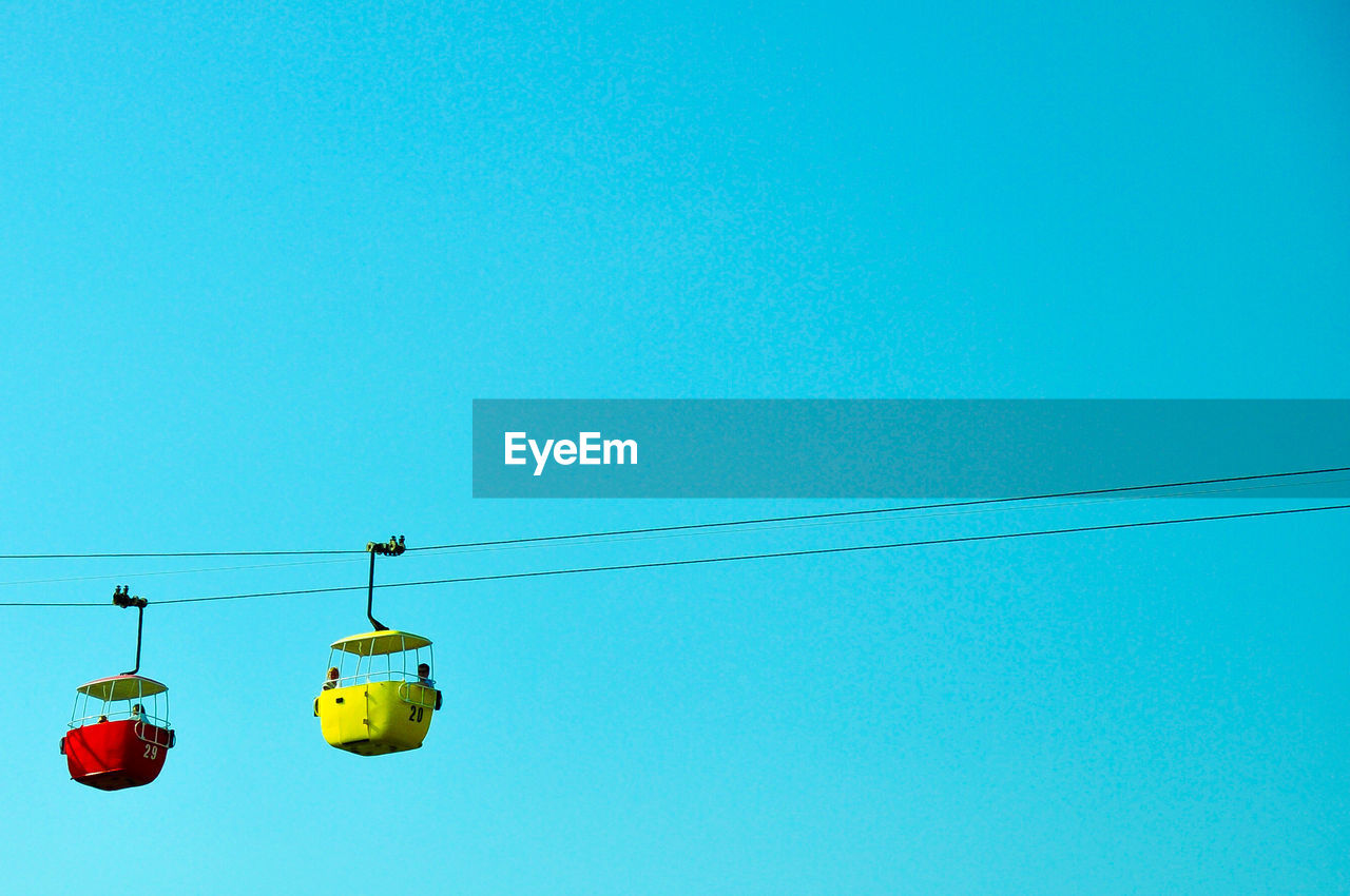 Low angle view of overhead cable cars against clear blue sky