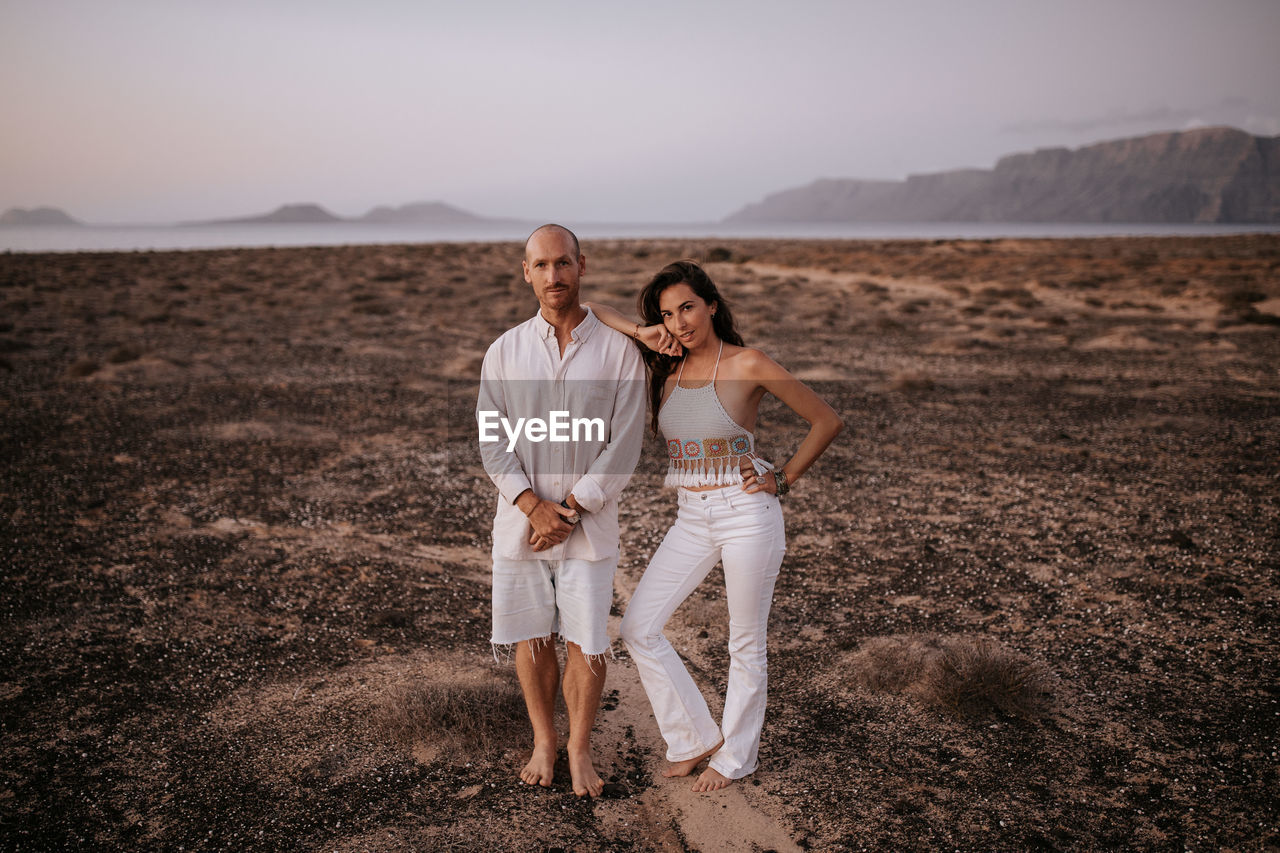 Peaceful couple in white outfit standing together in savanna and looking at camera