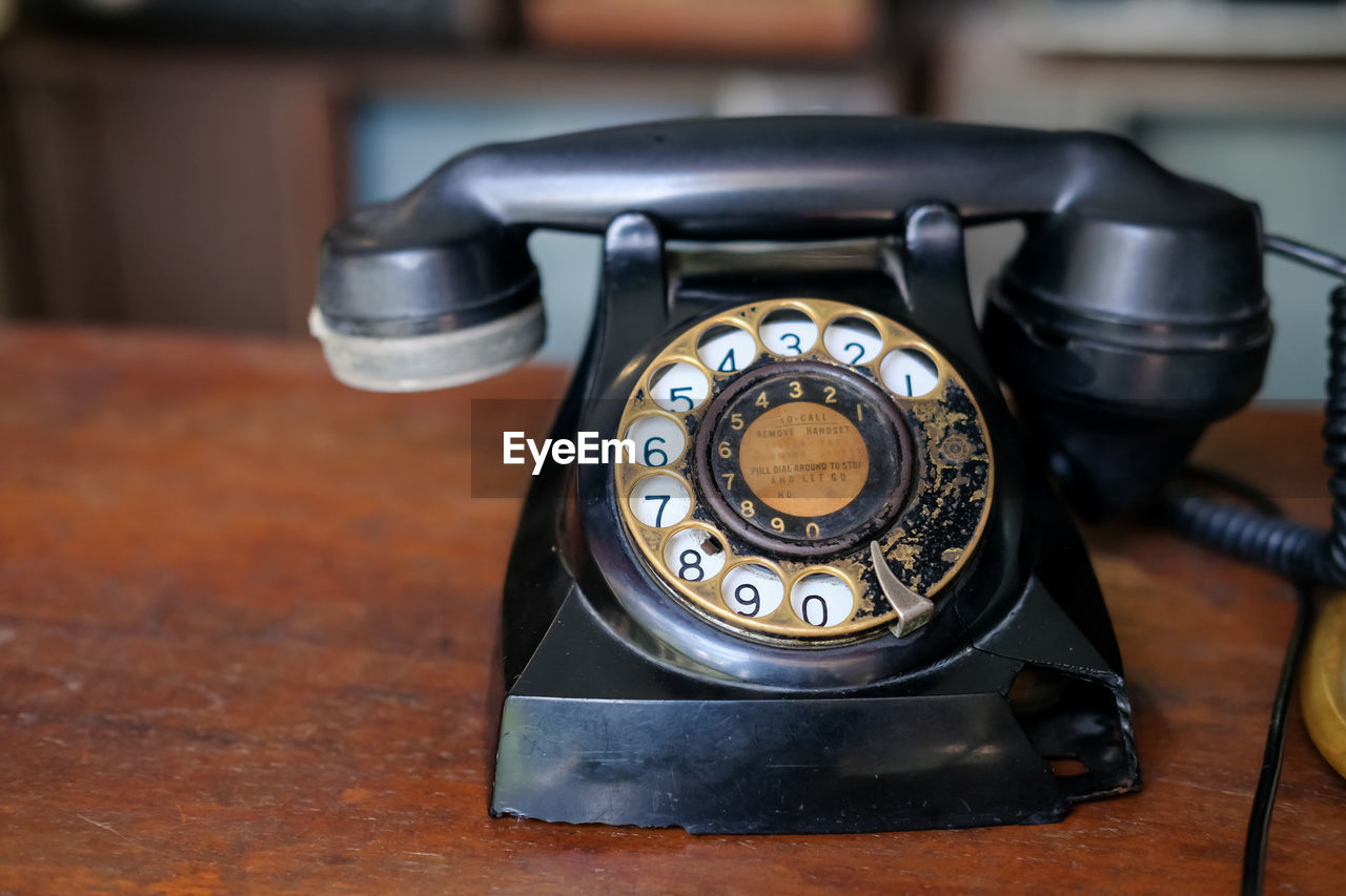 corded phone, telephone, rotary phone, landline phone, technology, retro styled, telephone receiver, communication, nostalgia, table, number, black, indoors, history, the past, old, close-up, no people, single object, focus on foreground, telephony, dial, telecommunications equipment, wood