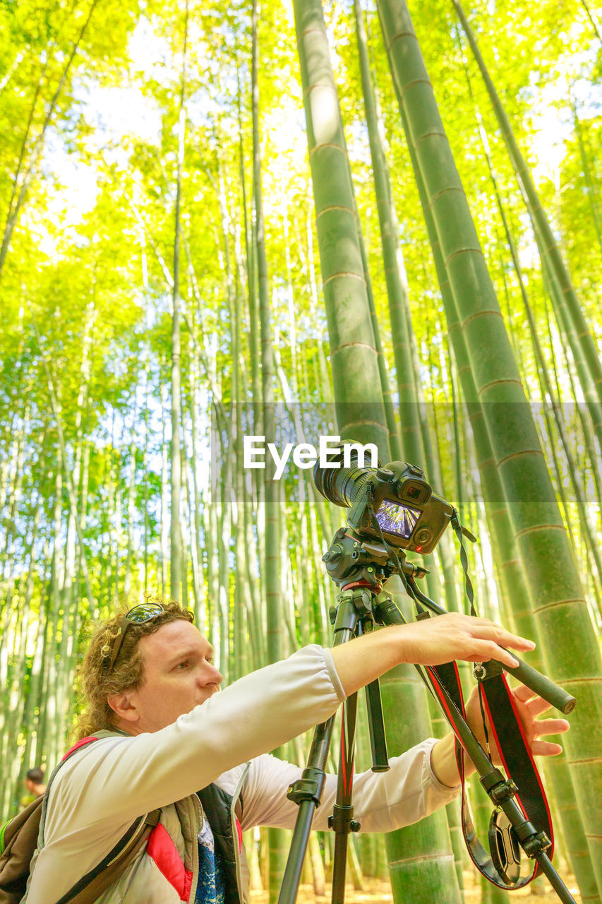 Man holding camera while standing amidst forest