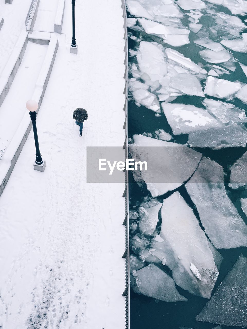 High angle view of man walking on snow covered pathway by icebergs in river