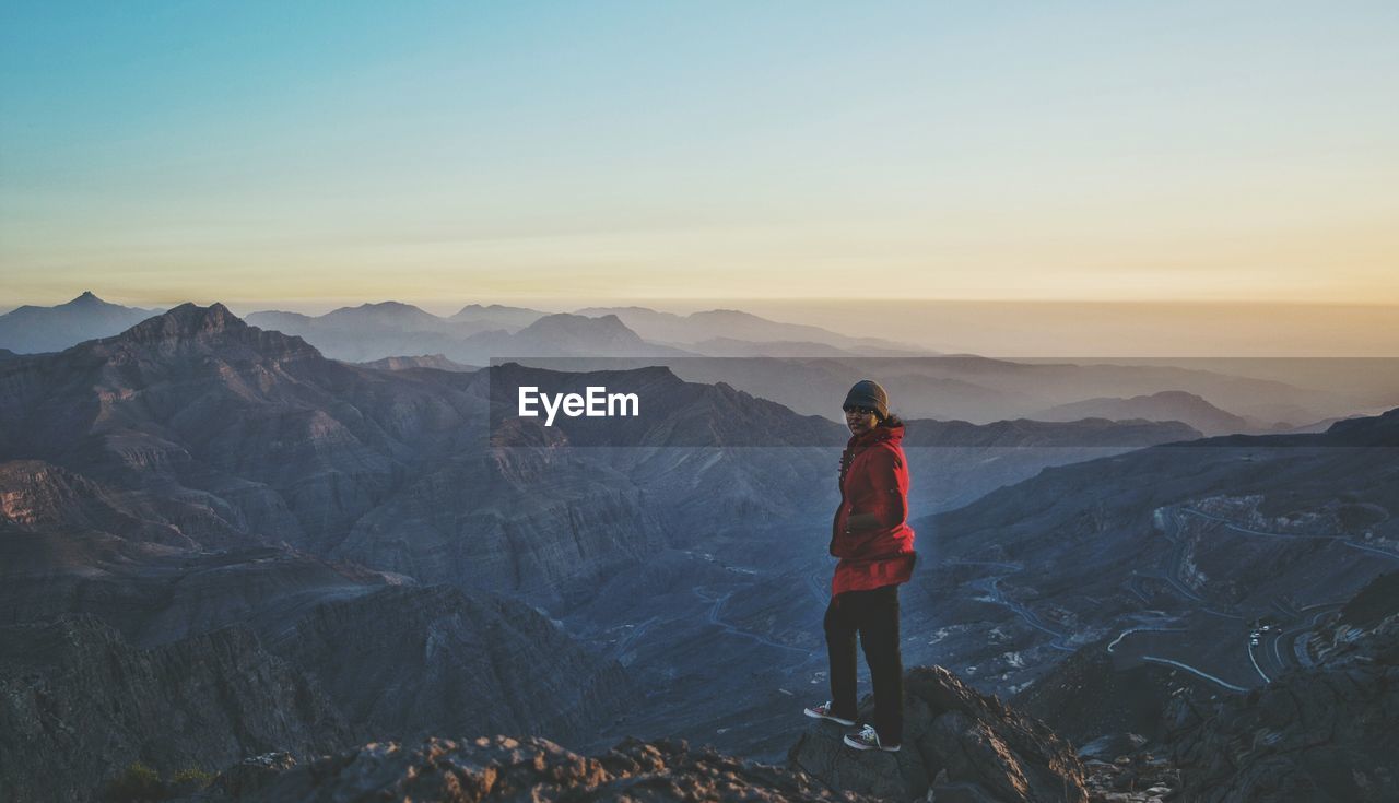 Portrait of woman standing on mountains against sky during sunset