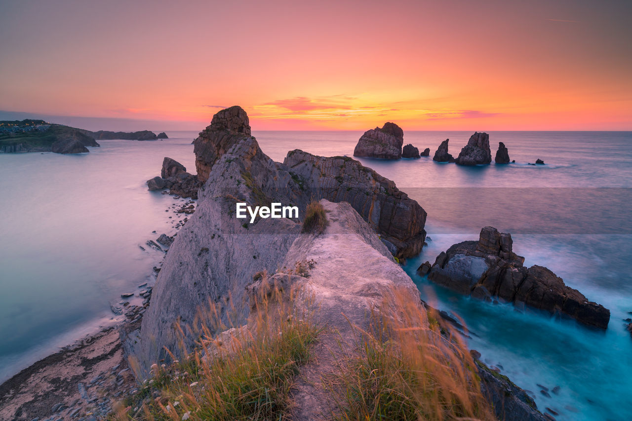 Breathtaking landscape of rocky cliffs in waving sea reflecting picturesque colorful sunset sky in cantabria