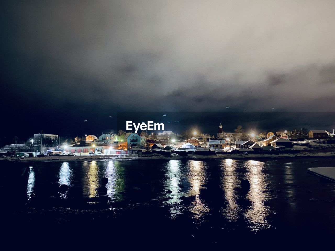 Illuminated city by sea against sky at night