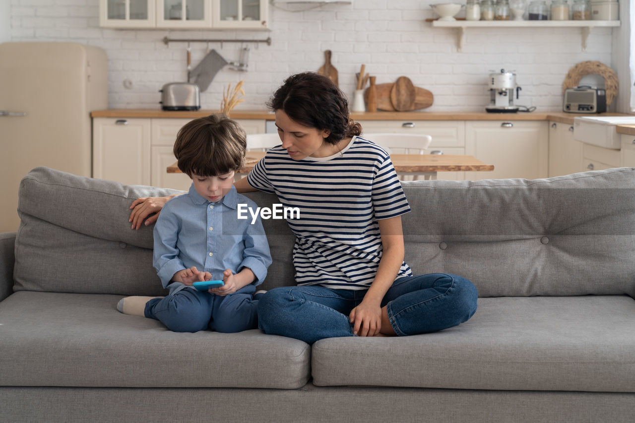 Son using mobile phone while sitting with mother at home