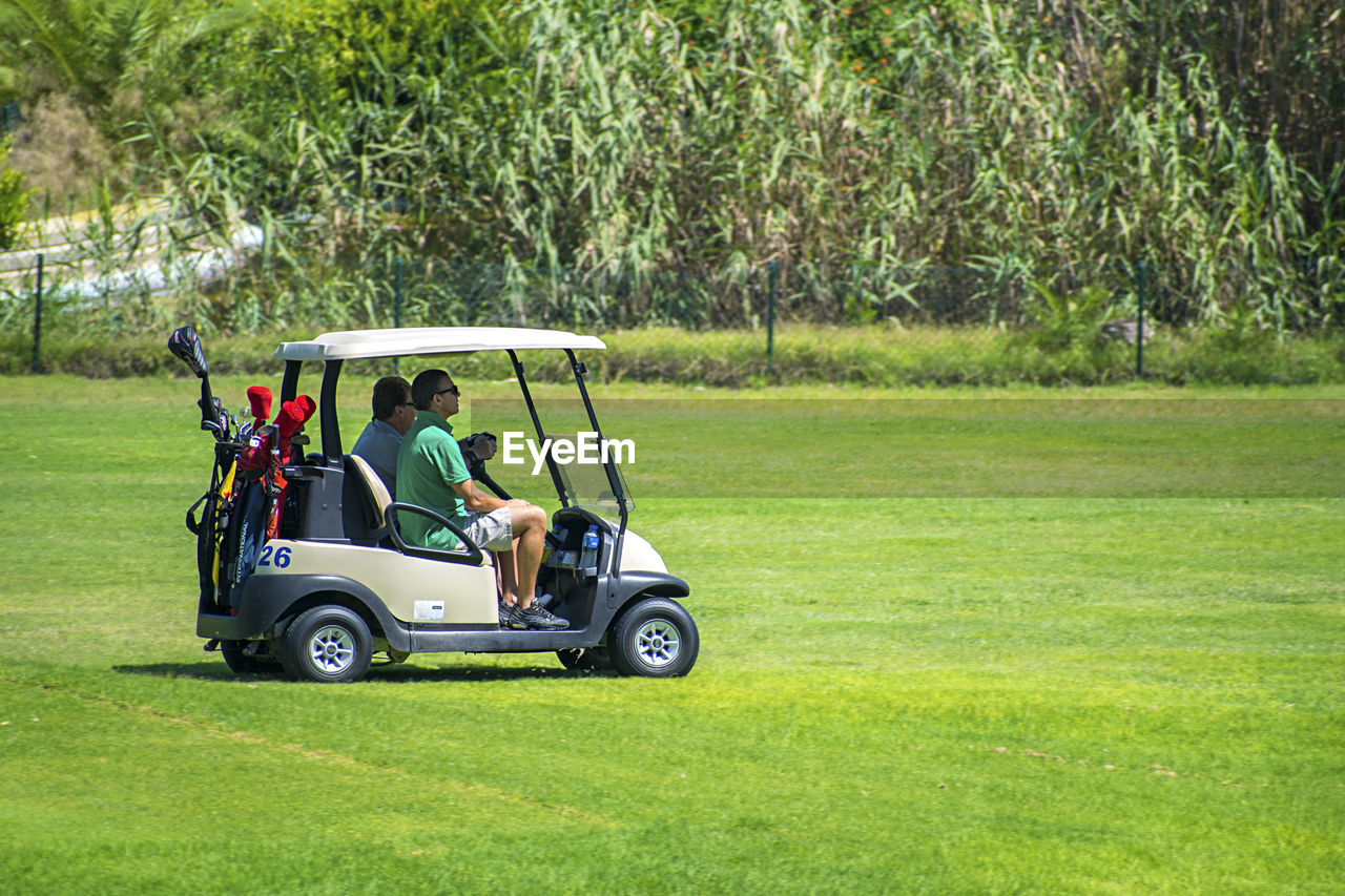 MAN SITTING ON GOLF COURSE AGAINST GREEN GRASS