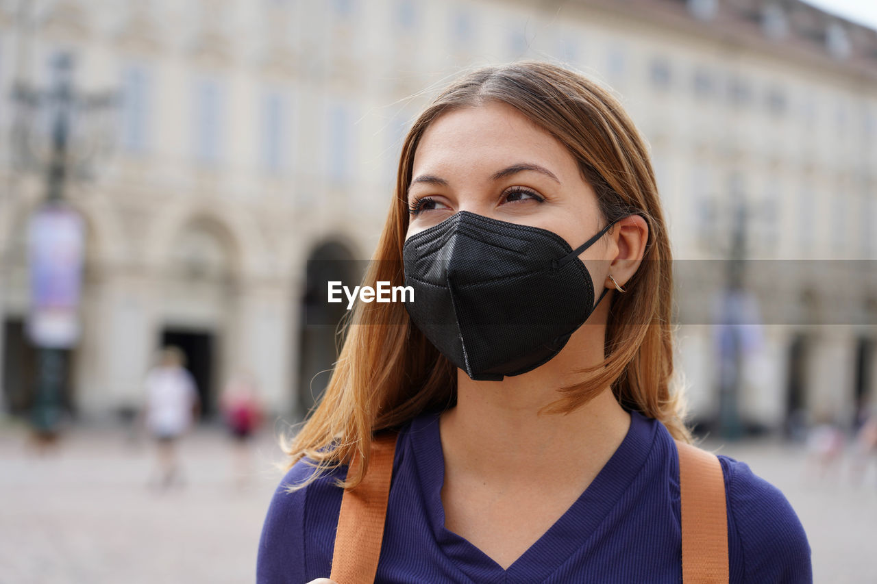 Portrait of student girl wearing a protective kn95 ffp2 black mask walking in city street