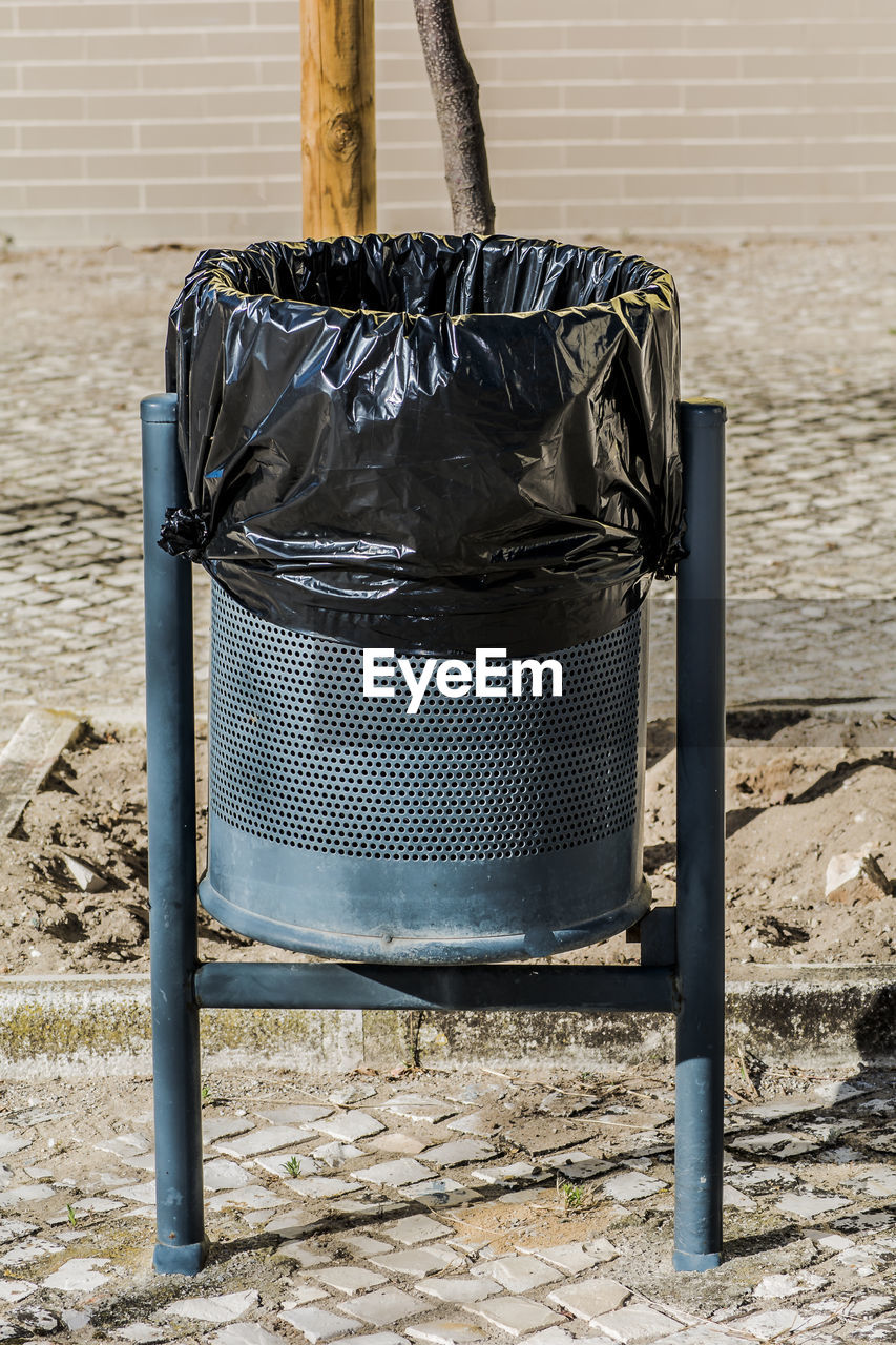 Close-up of garbage bin on footpath against wall