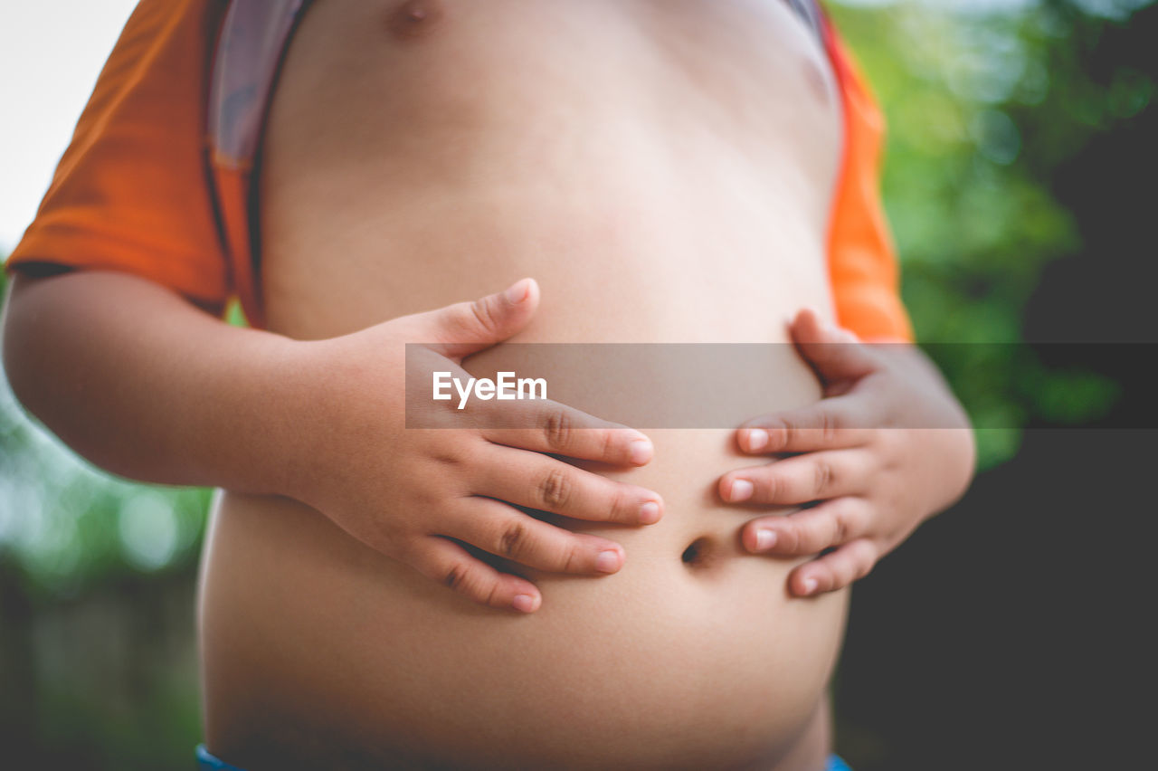 Midsection of boy touching his stomach outdoors