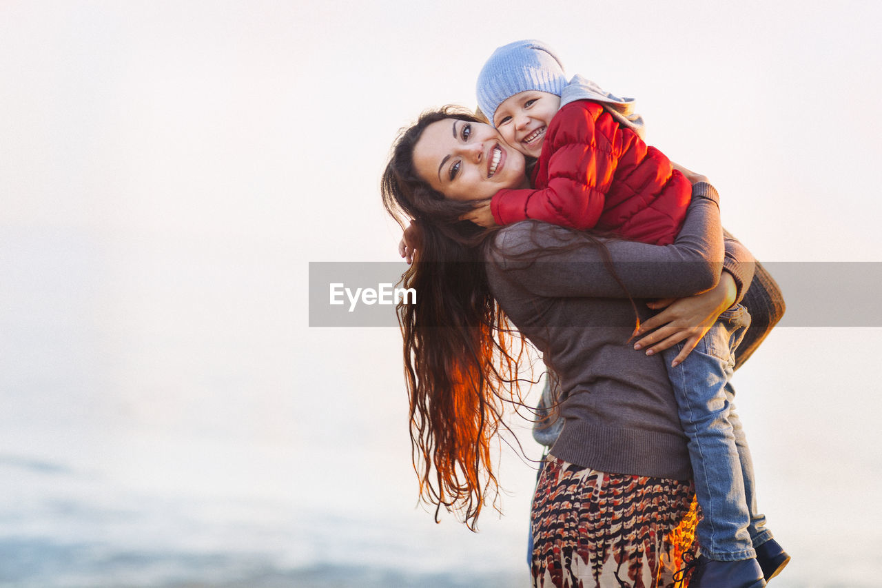 Mother holding daughter in arms against clear sky