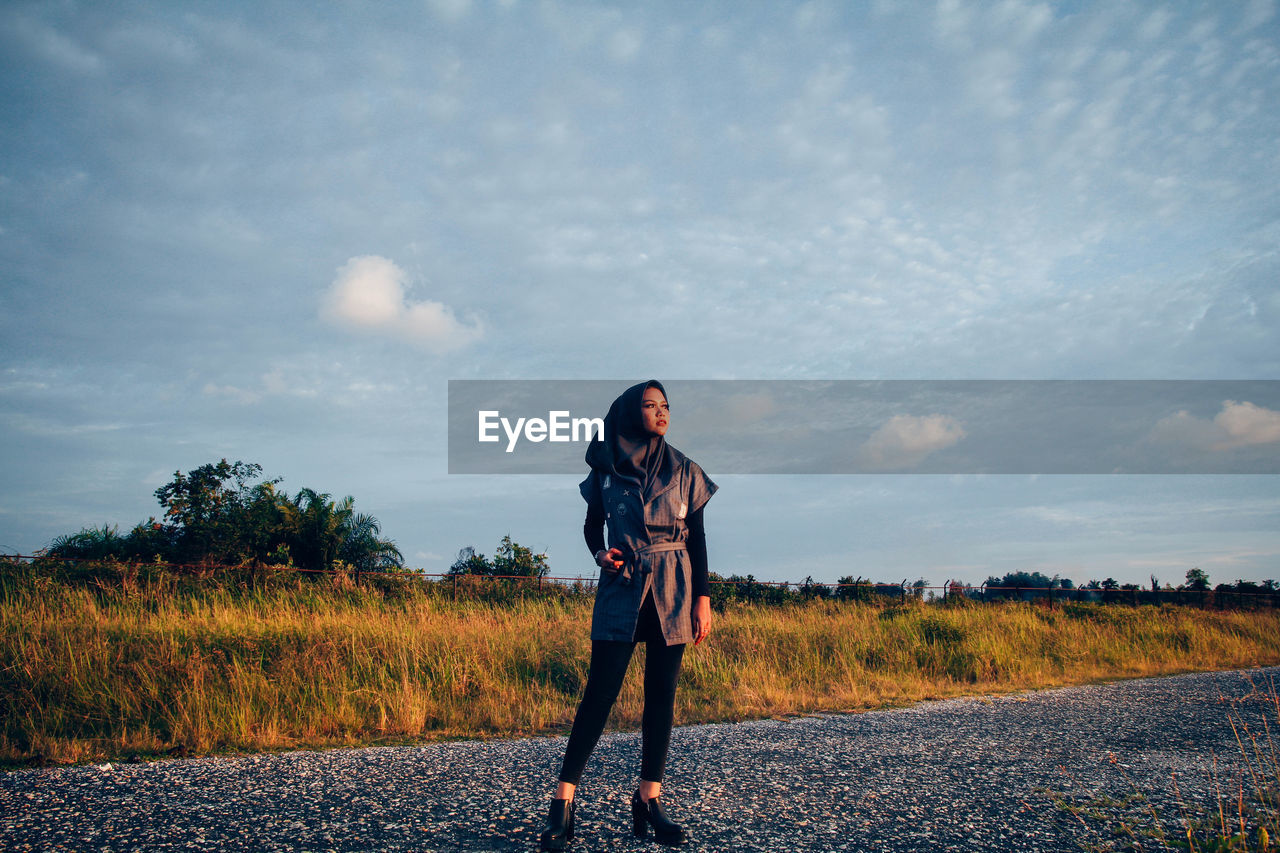 Full length of woman looking away while standing on road against sky