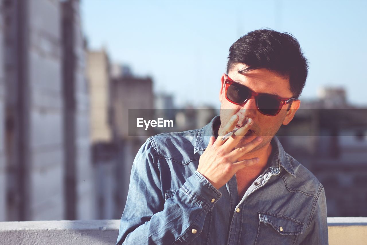 Portrait of man in sunglasses smoking cigarette against buildings