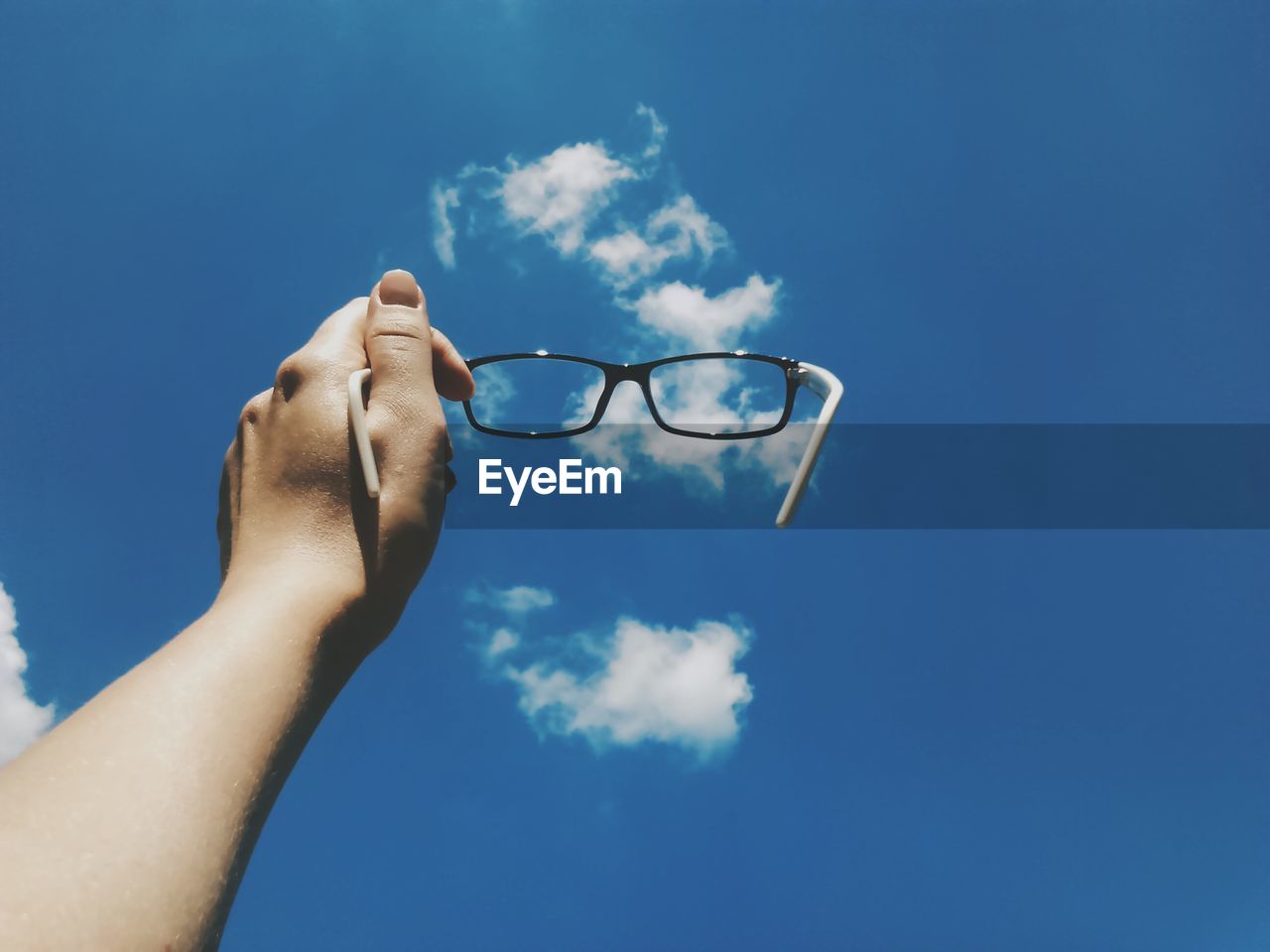 Cropped image of hand holding eyeglasses against blue sky
