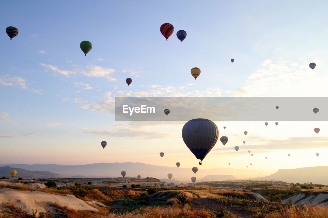 Hot air balloons flying over landscape against sky during sunset