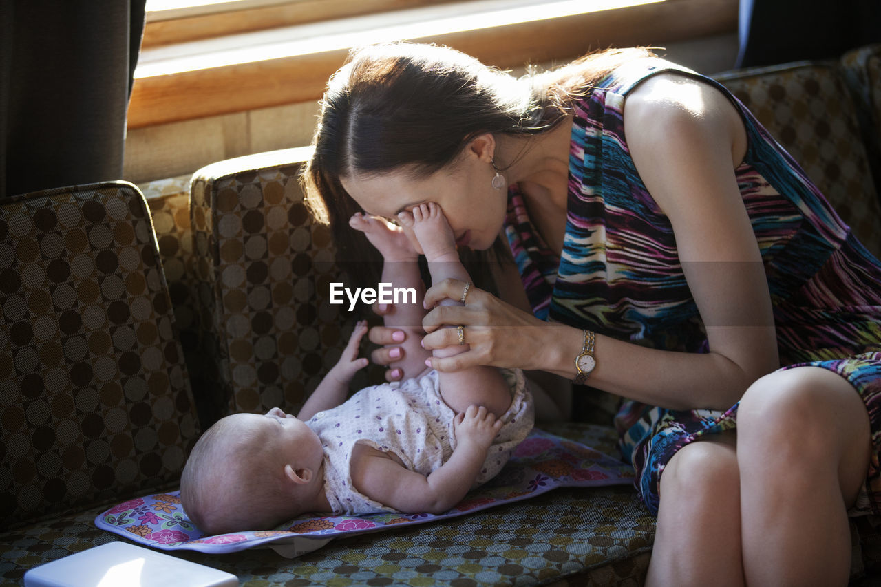 Woman playing with baby girl on sofa at home