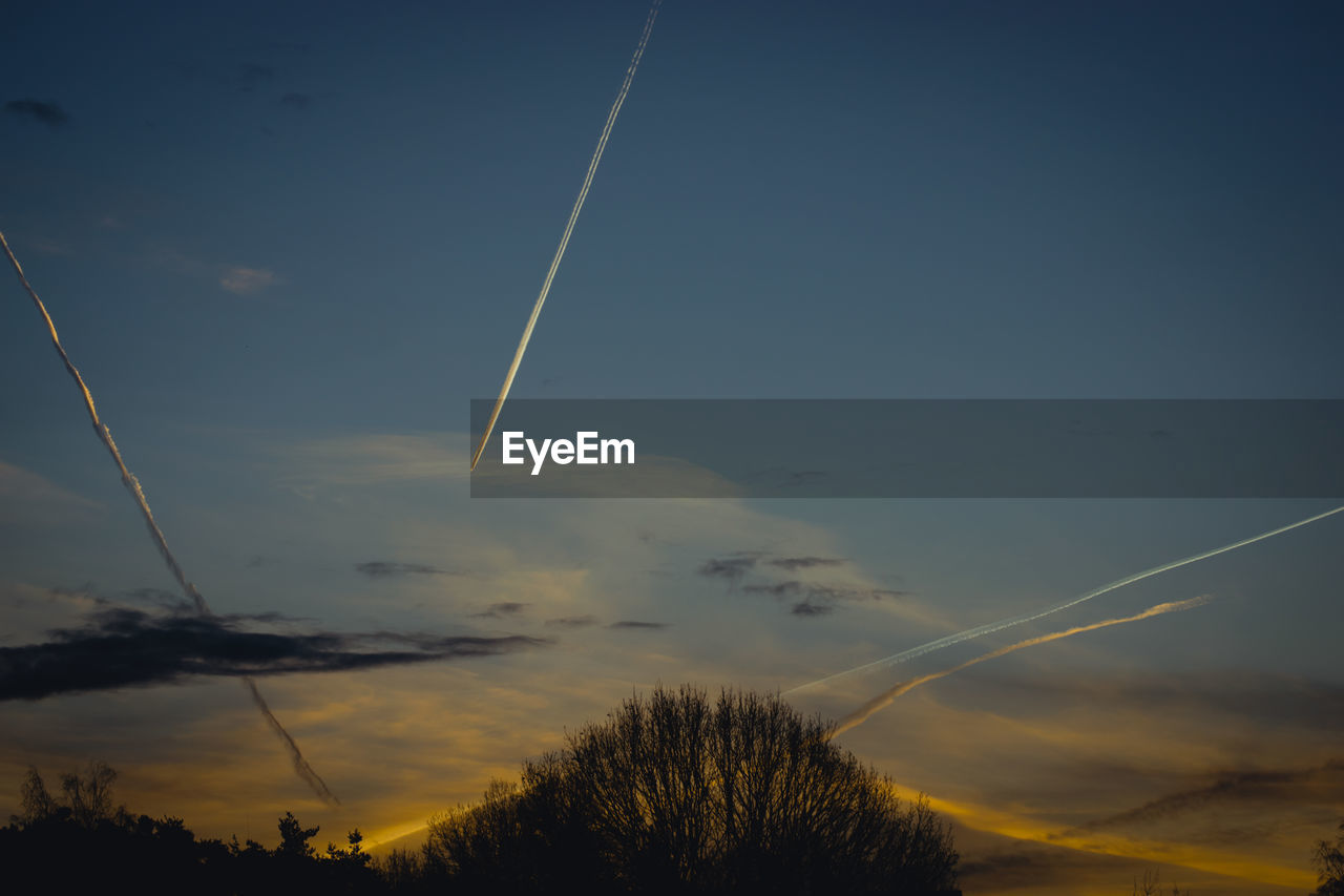 LOW ANGLE VIEW OF VAPOR TRAILS IN SKY AT SUNSET