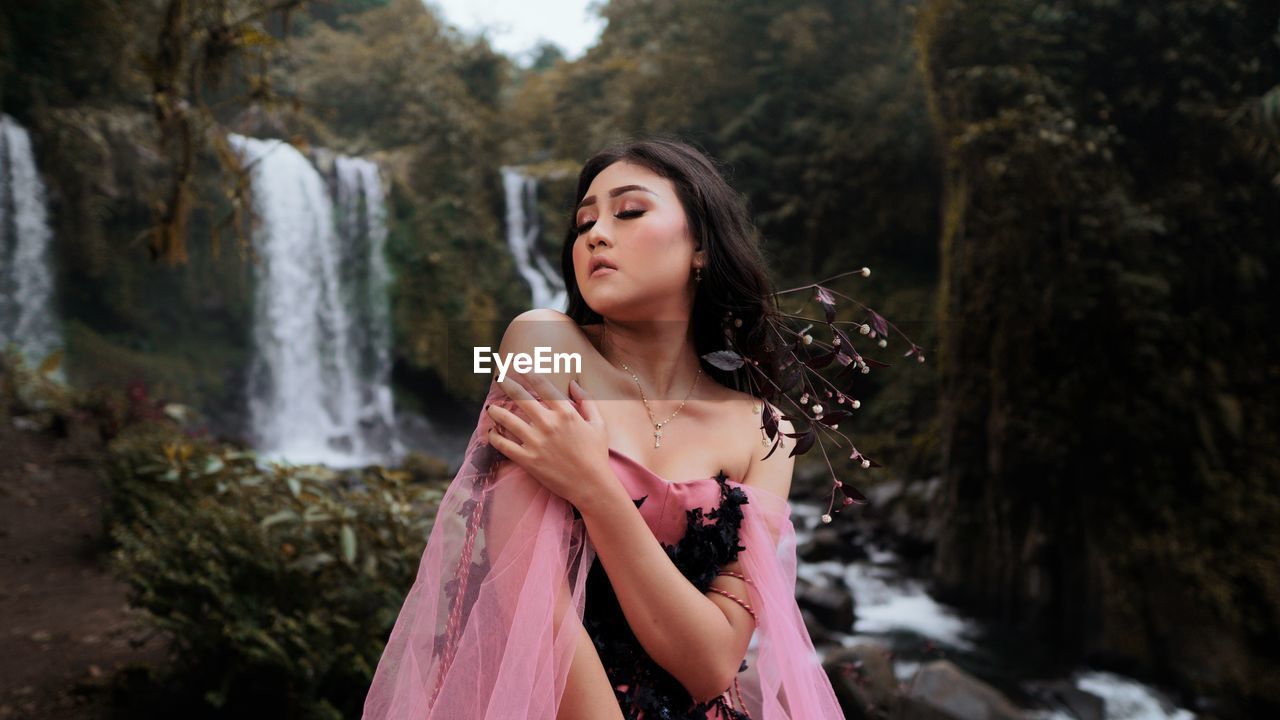 Beautiful young woman standing against waterfall