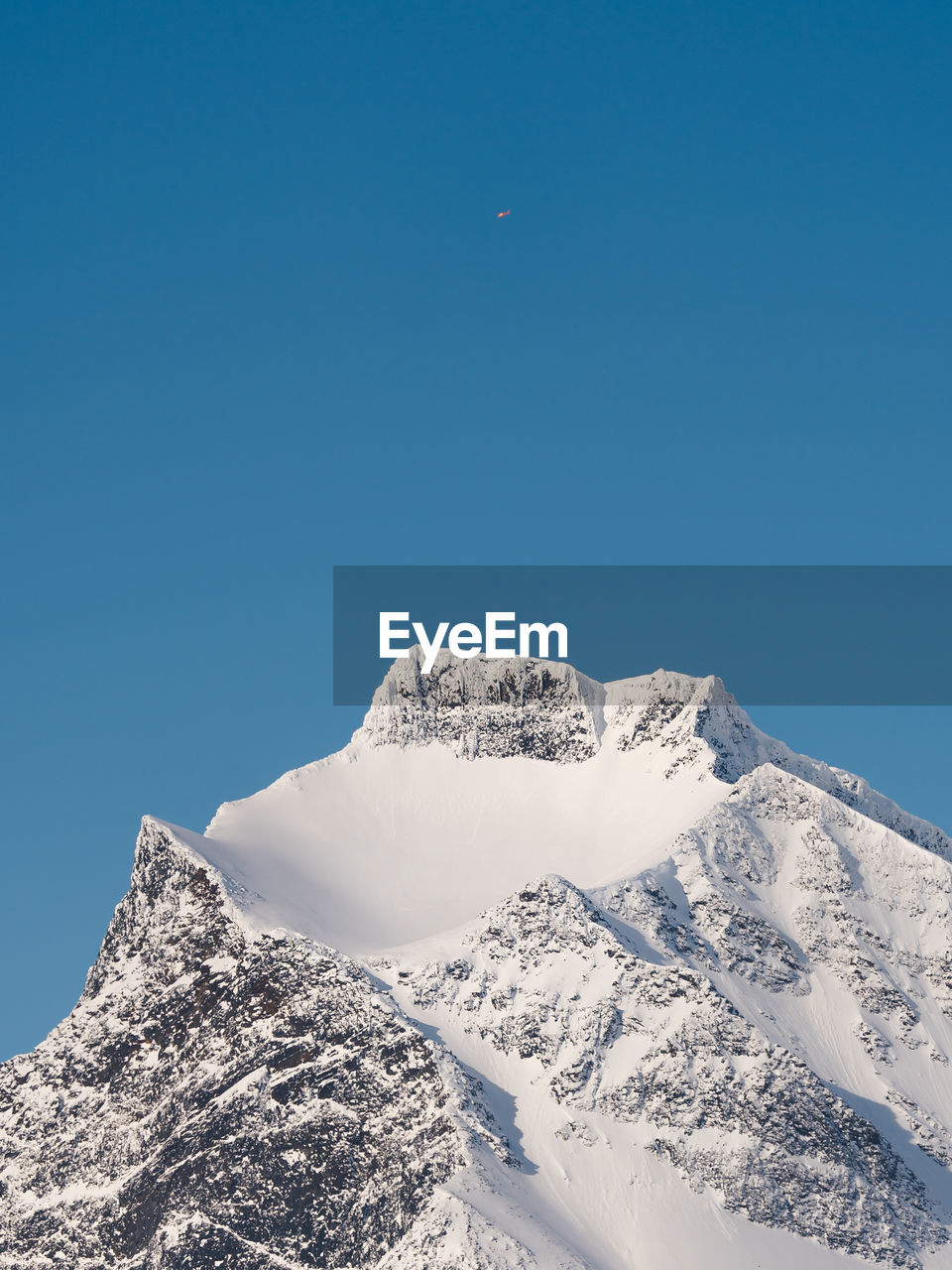 Low angle view of snowcapped mountain and helicopter against clear blue sky 