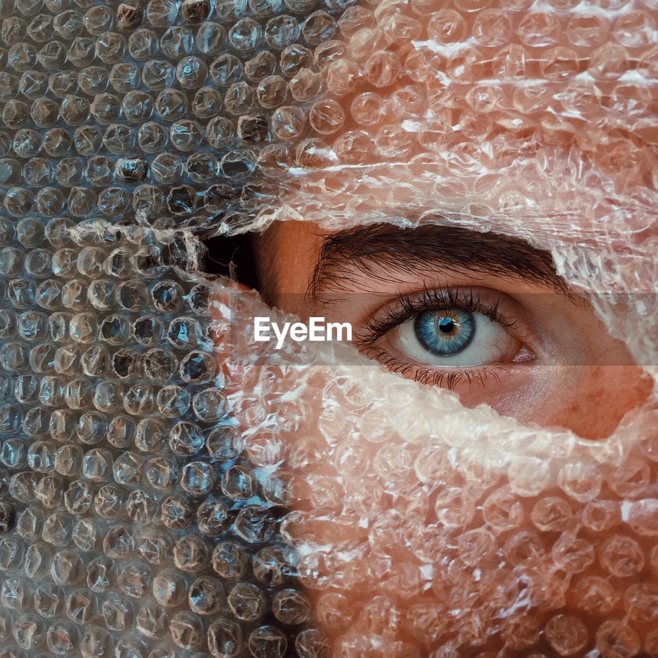 Close-up portrait of boy peeking through hole in bubble wrap