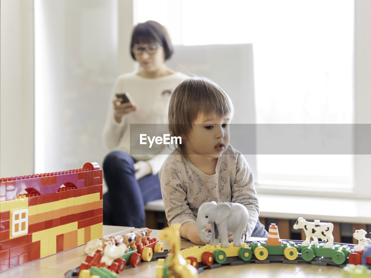 Boy plays with toy blocks. his mother or babysitter texting in smartphone.kindergarten or nursery.