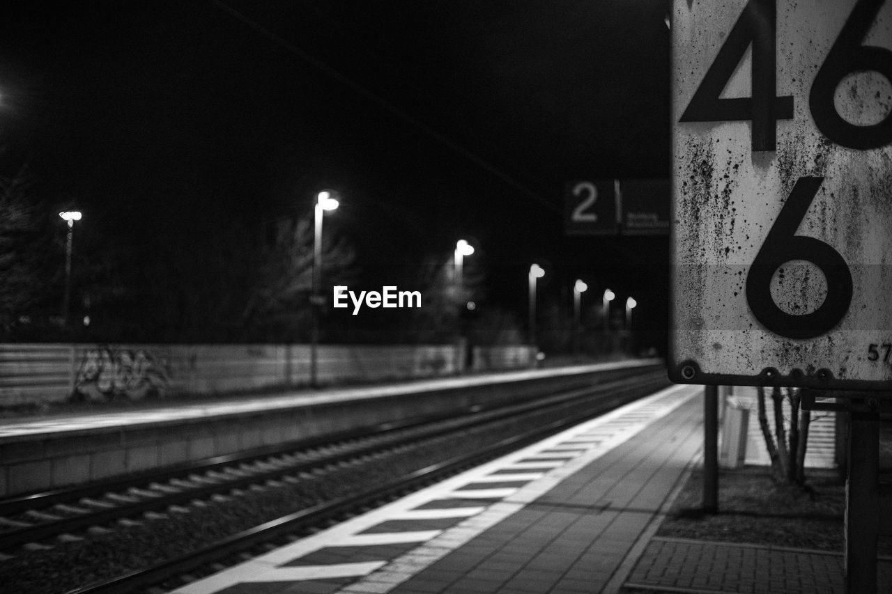 RAILROAD TRACKS AT ILLUMINATED STATION AT NIGHT