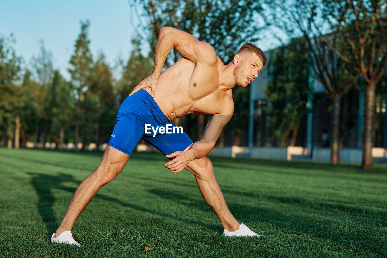 Full length of shirtless man sitting on grass